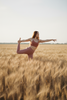 Woman in terracotta and dusty rose activewear doing a yoga pose in a wheat field